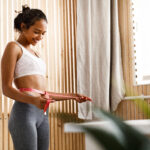 African woman is measuring her waist with a centimeter and smiles
