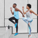 Hard sport concept. Motion shot of two black female and male run up steps, demonstrate good ability of climbing high, have bottles with fresh water to prevent dehydration, move against white wall